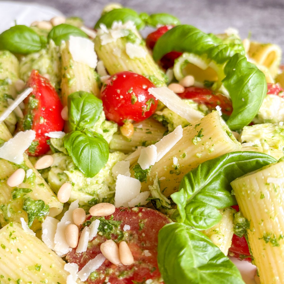 Close-up pesto pasta salad, halved cherry tomatoes, torn mozzarella, pine nuts and basil