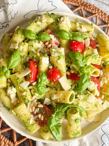 Summer pesto pasta salad served in a white bowl on a woven rattan mat with basil on top