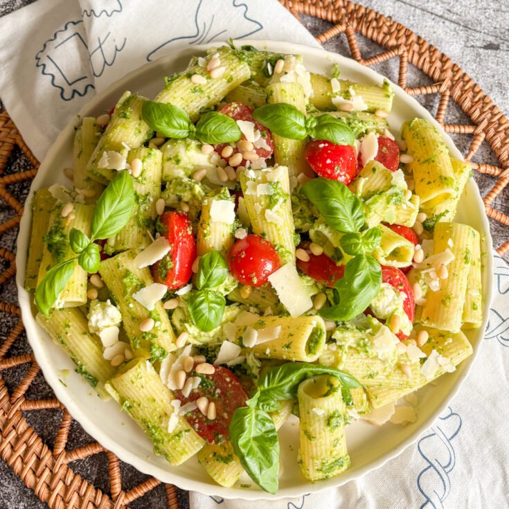 Summer pesto pasta salad served in a white bowl on a woven rattan mat with basil on top