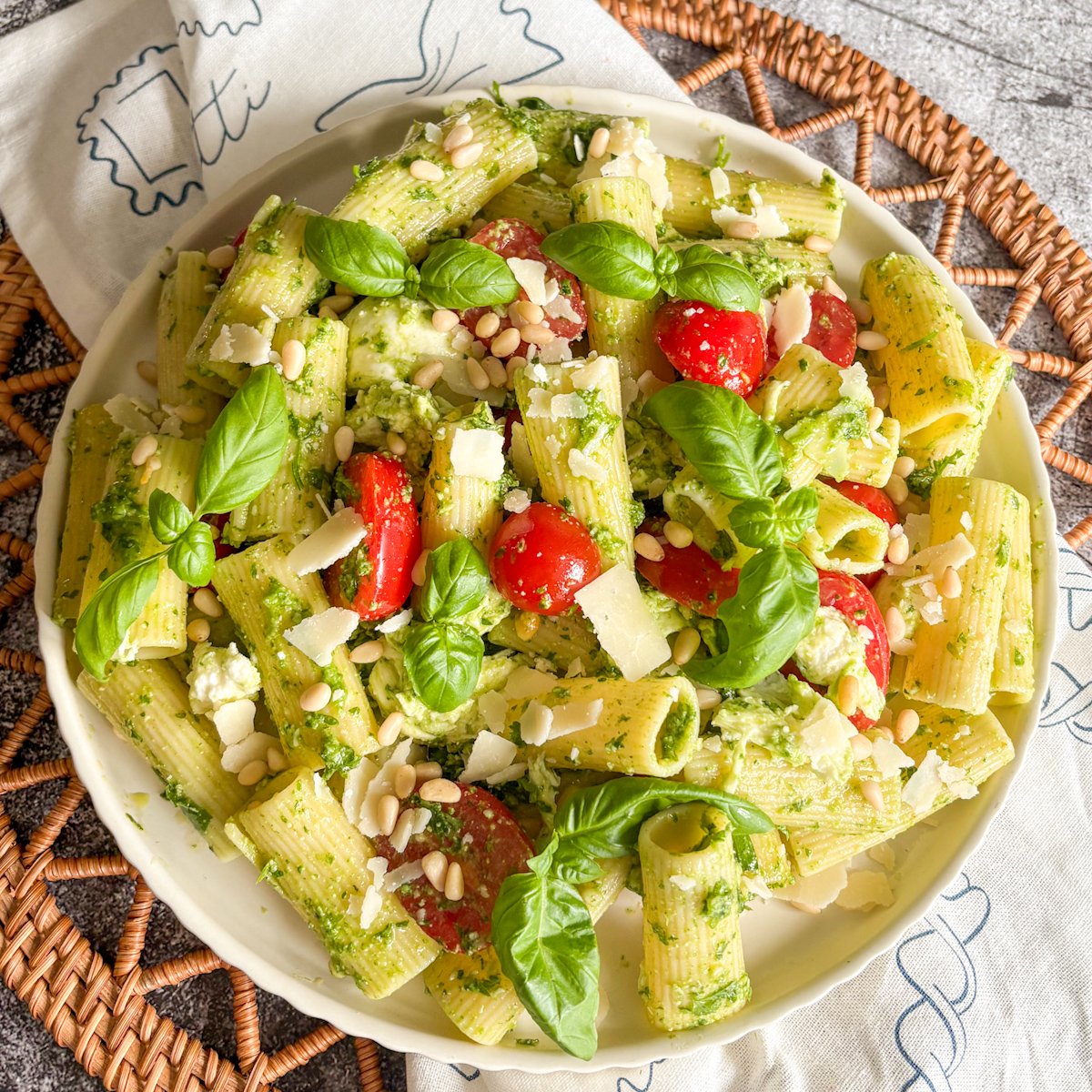 Summer pesto pasta salad served in a white bowl on a woven rattan mat with basil on top