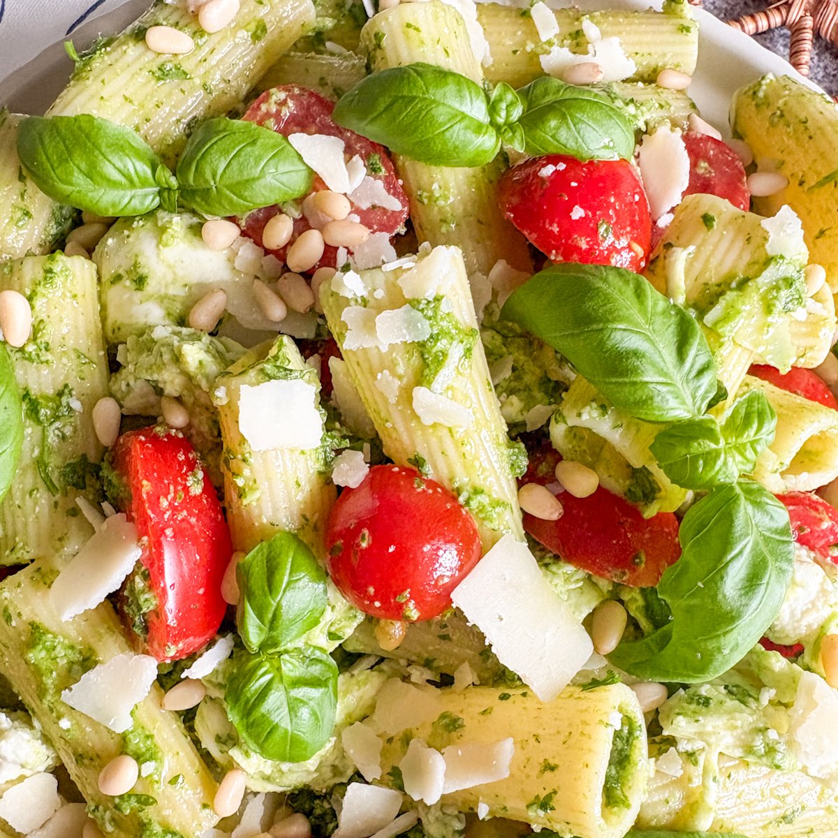 Close-up parsley pesto pasta salad with rigatoni, juicy tomatoes, pine nuts and basil sprigs
