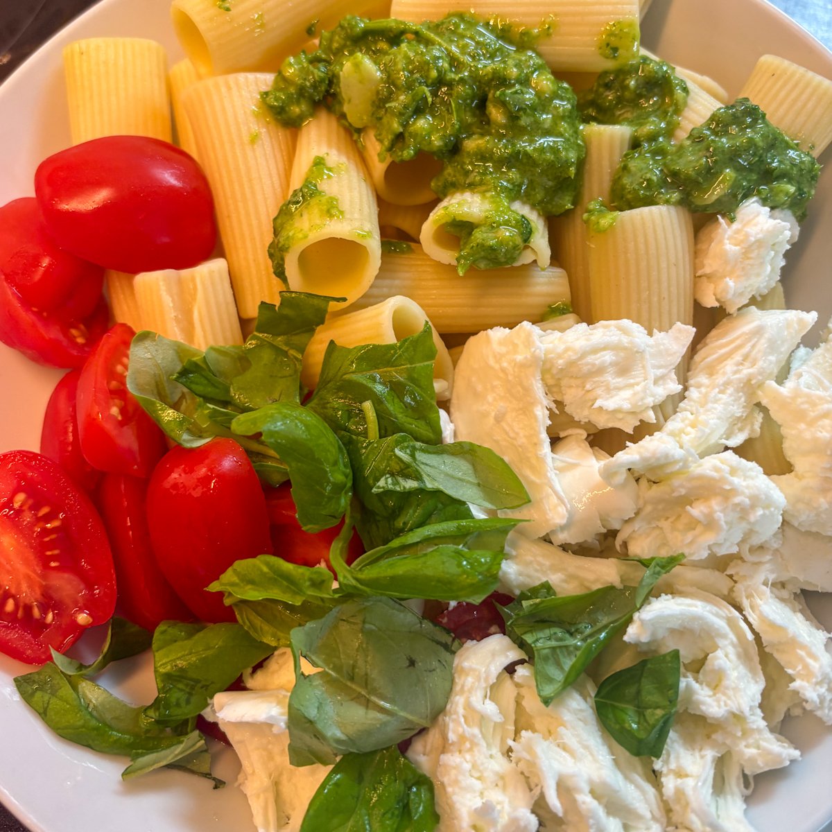 Rigatoni, halved tomatoes, torn mozzarella and green pesto in a bowl before mixing