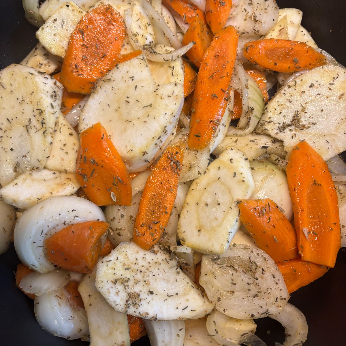 Chicken legs with vegetables prep — sliced carrots, parsnips and onion tossed in herbs in a pan