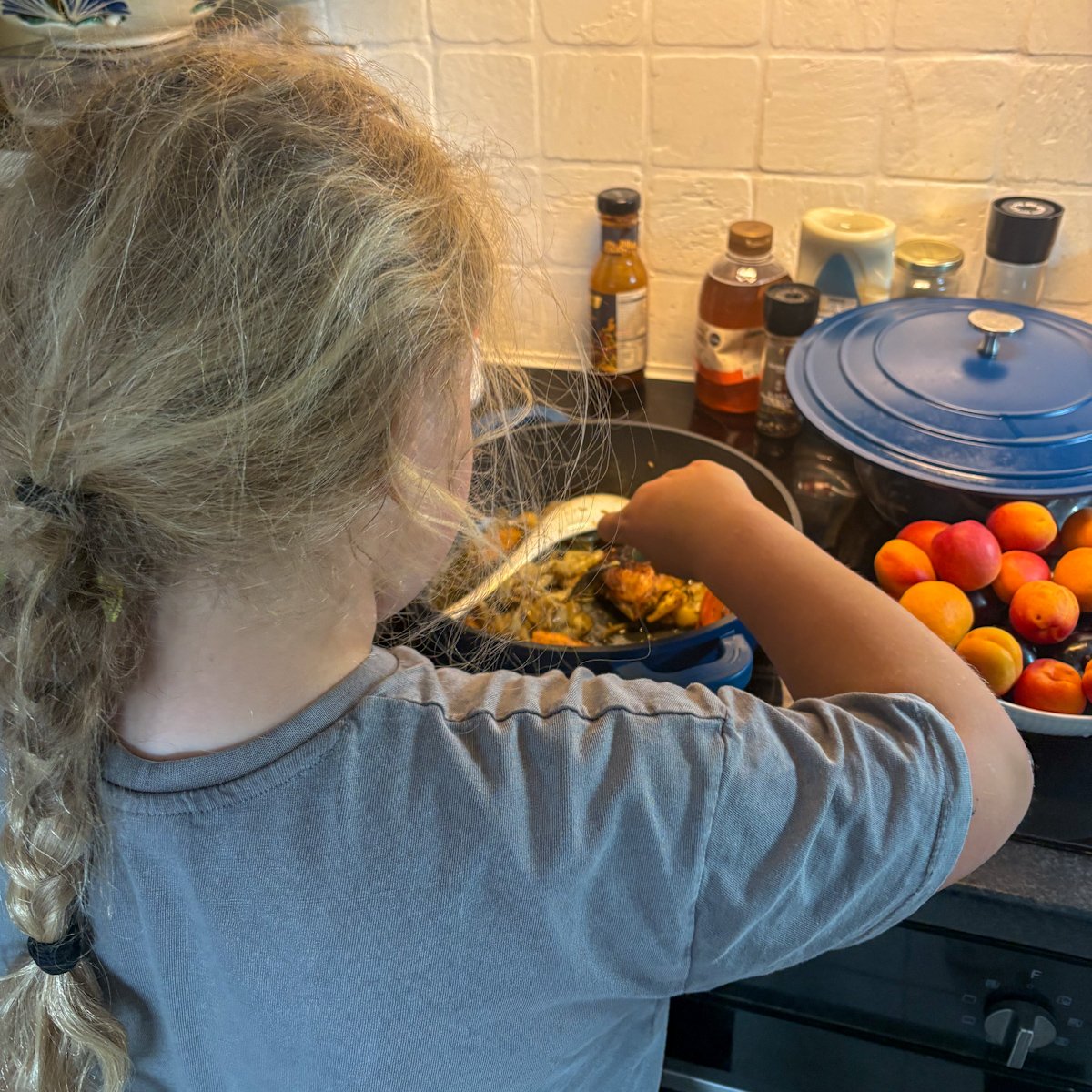 Child picking sweet roasted vegetables straight from the skillet of chicken legs with vegetables