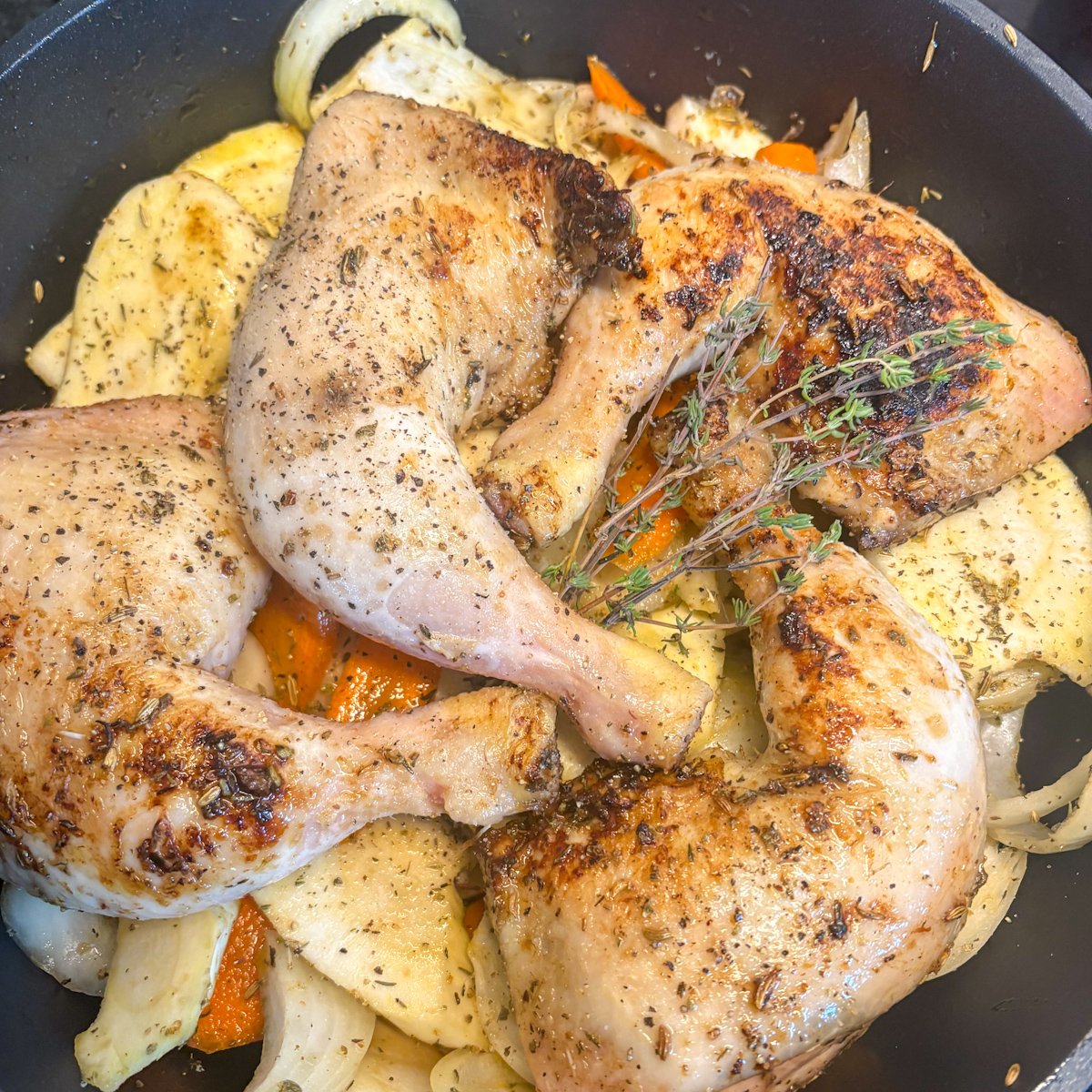 Golden seared chicken legs with vegetables and thyme roasting in a dark skillet