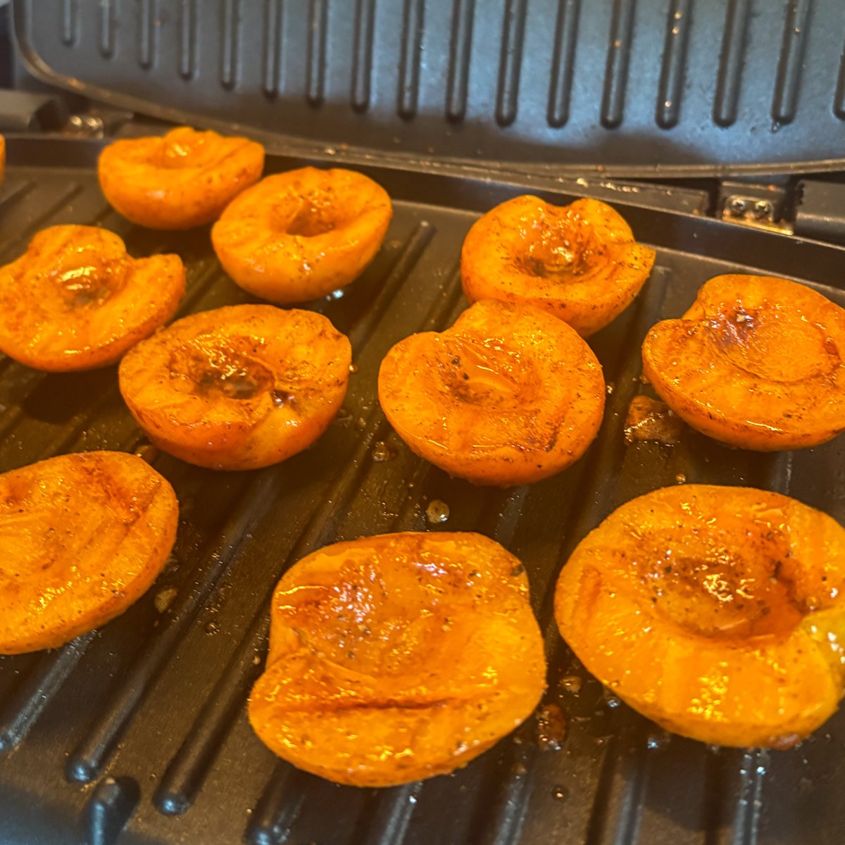 Grilled apricot halves on a hot grill, cut sides caramelised and glossy with sweet, spiced juices