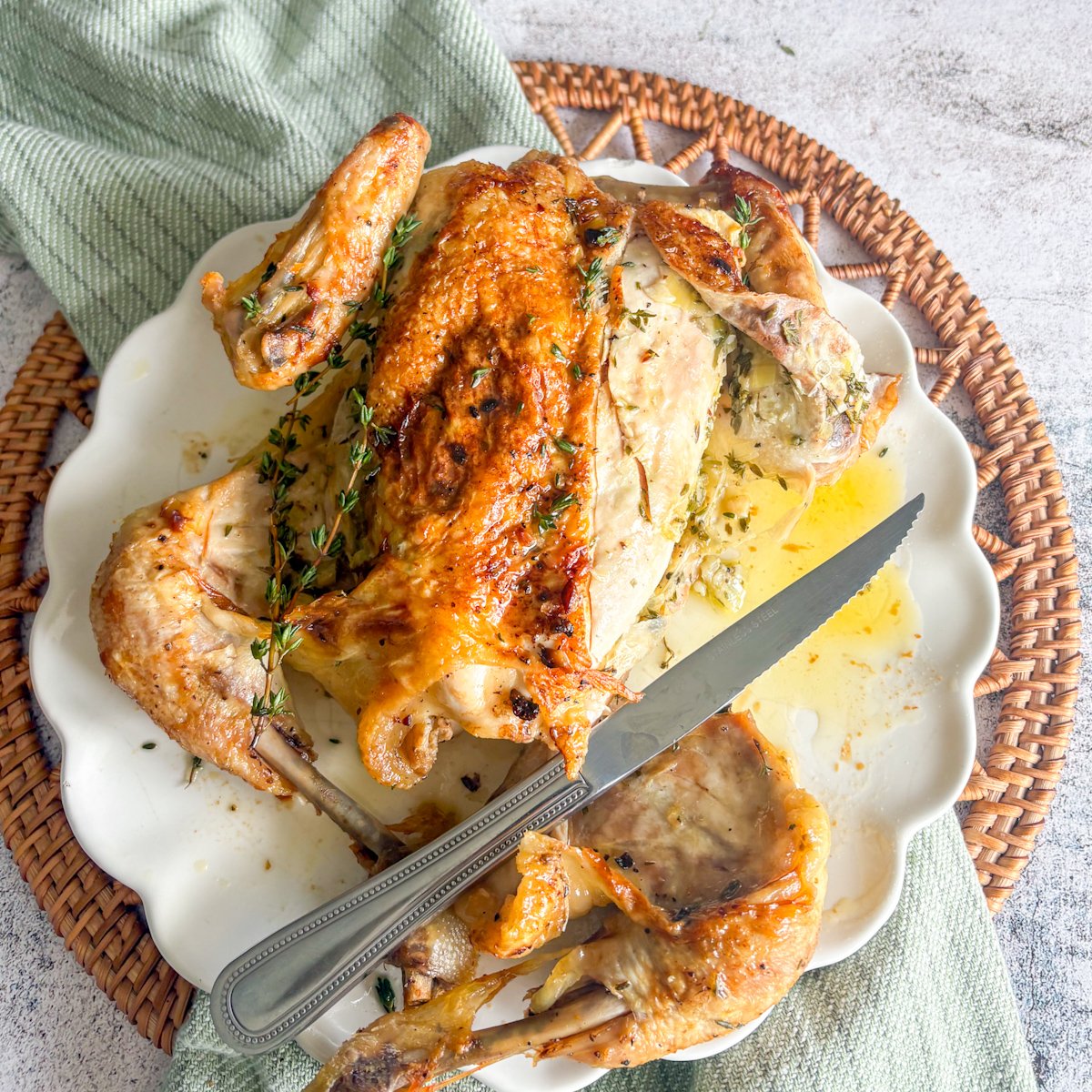 Overhead view of herb butter roast chicken being carved, one breast sliced open to show the herb butter layer under the skin, with a knife, thyme sprigs and buttery juices on the plate.