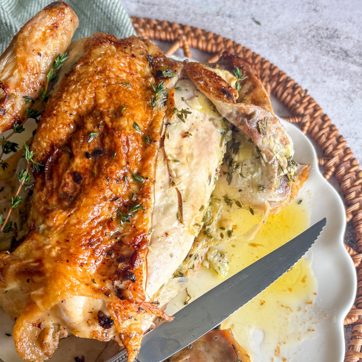 : Herb butter roast chicken partly carved on a white plate, showing juicy white breast meat under the golden skin with visible flecks of green herb butter and pooled melted butter alongside.