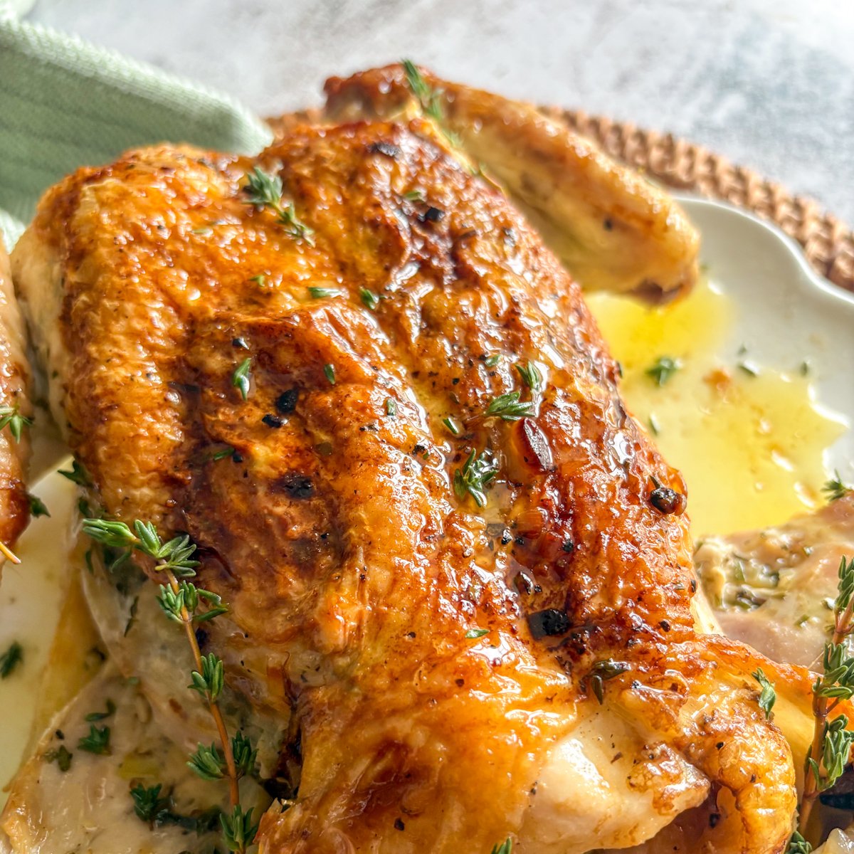 Close-up of the crisp, deeply golden breast of herb butter roast chicken with melted butter running across the skin, sprigs of fresh thyme and cracked black pepper visible on the surface.