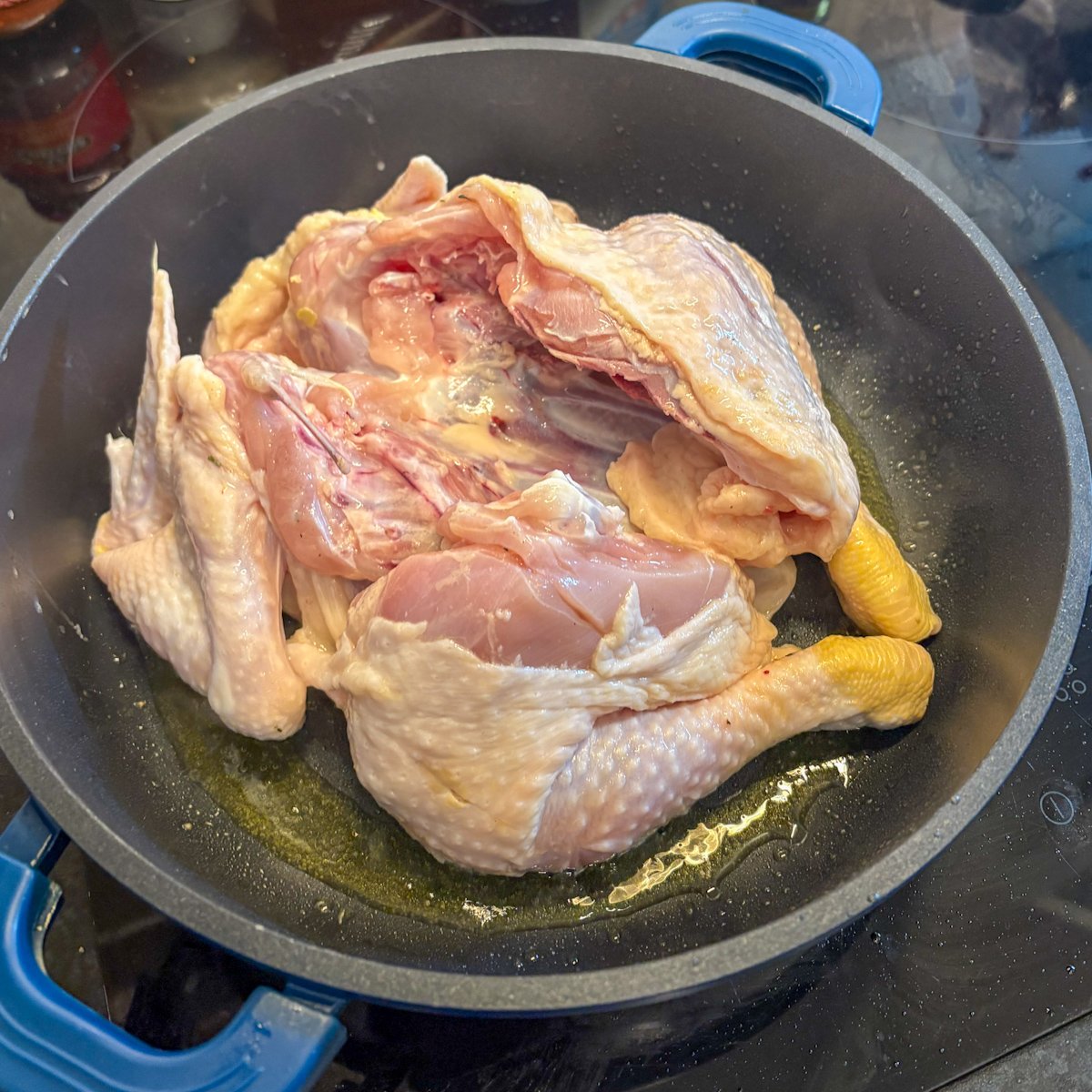 Raw spatchcocked chicken laid breast side down in a hot skillet with olive oil, ready to sear the first side before the herb butter roast chicken goes into the oven.