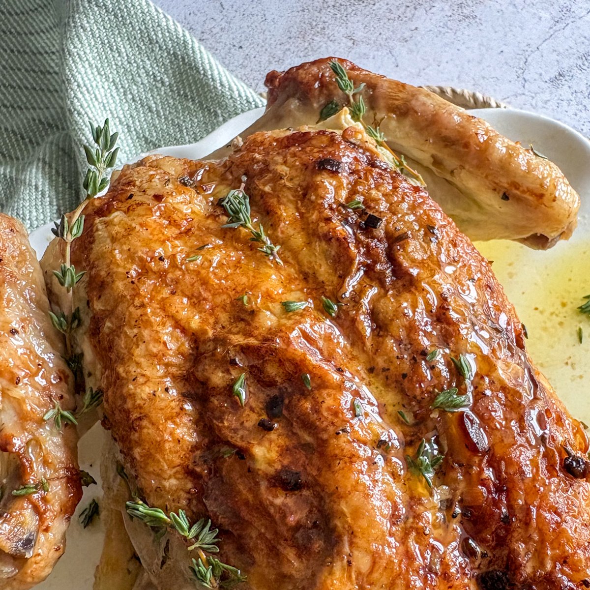 Close overhead shot of herb butter roast chicken with crackly bronzed skin, a wing resting in a pool of melted herb butter and thyme sprigs tucked around the meat.