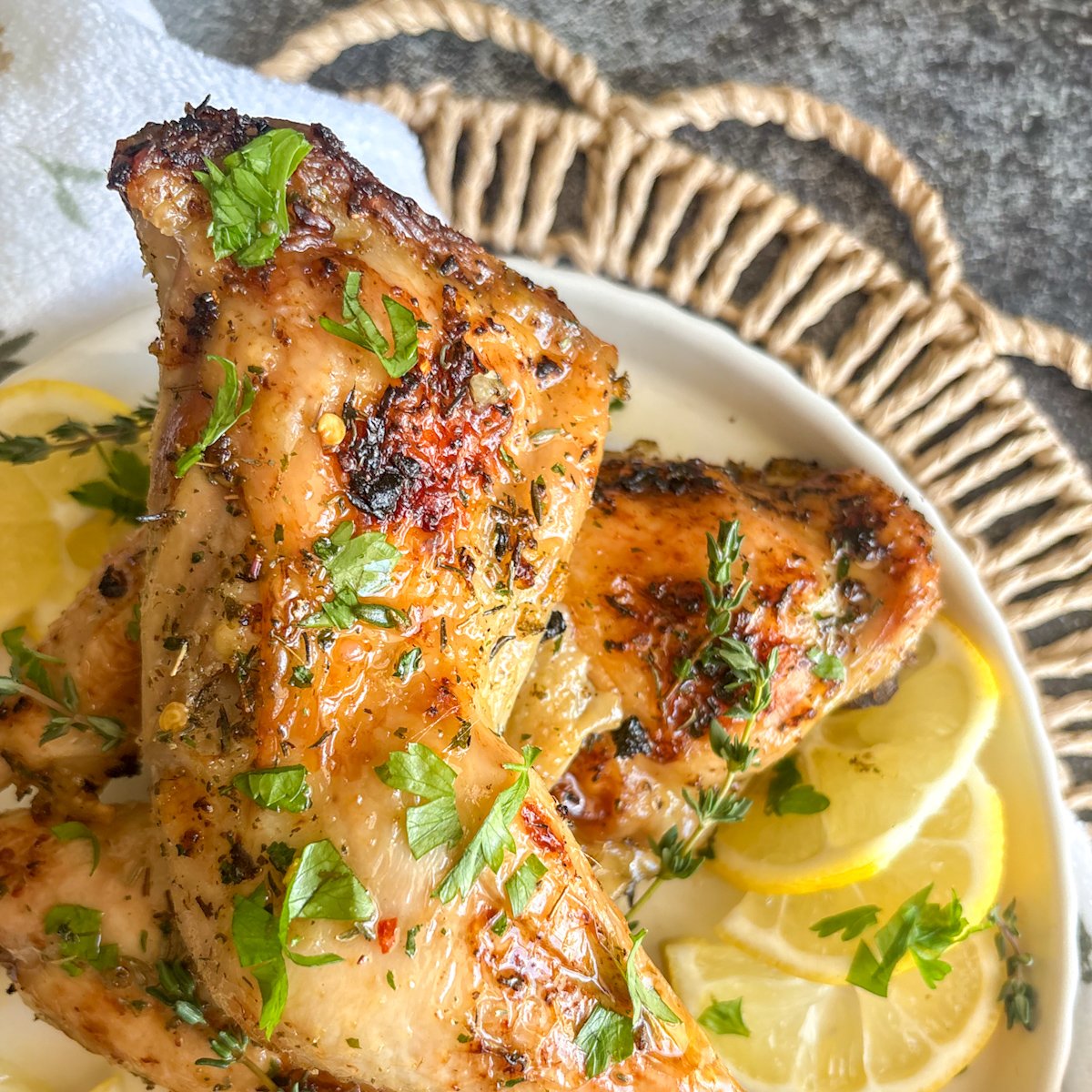 Close, angled shot of juicy lemon chicken legs with a glossy honey butter glaze, garnished with fresh parsley and thyme sprigs and surrounded by thin lemon slices on a pale plate, capturing the caramelised, sticky skin of this simple weeknight chicken recipe.