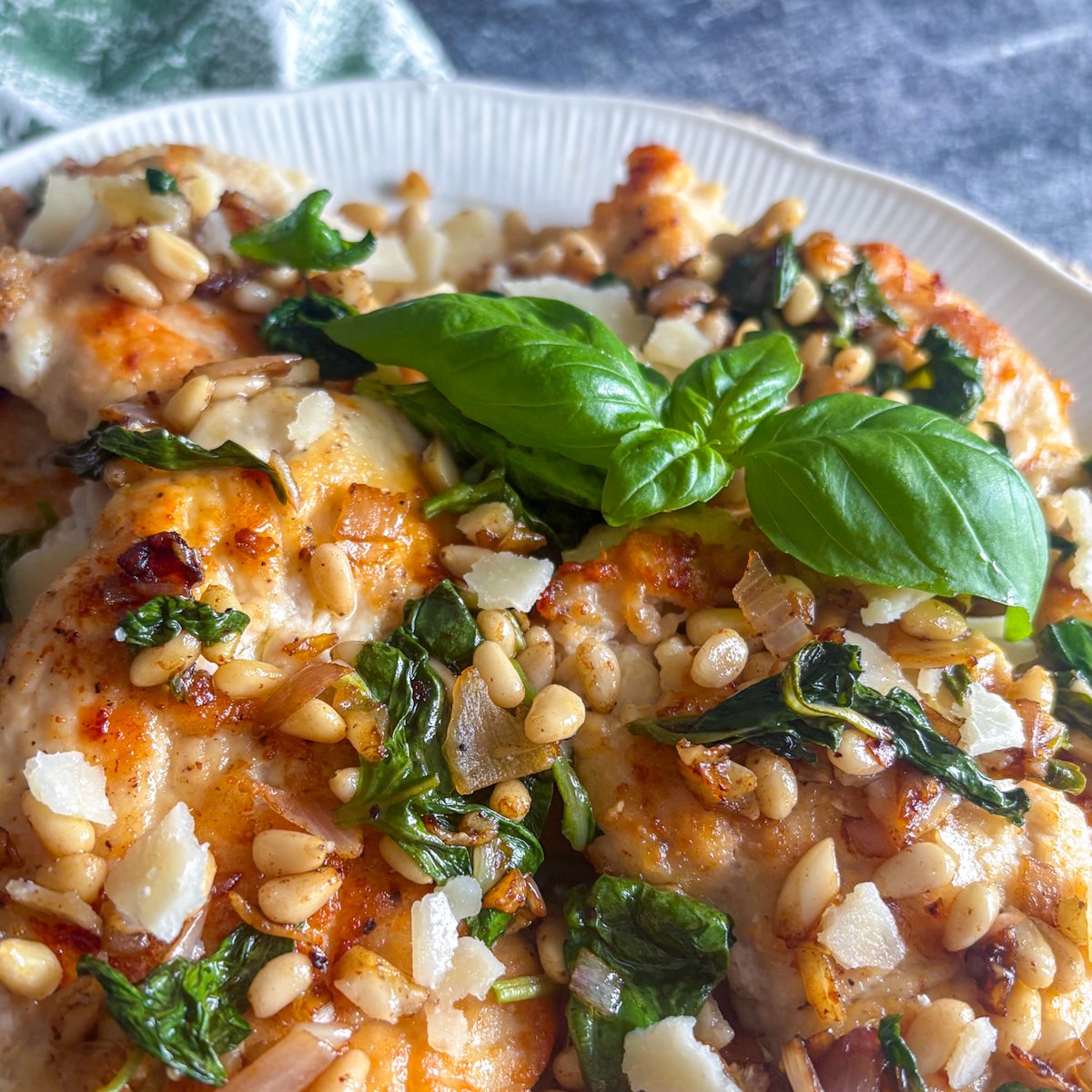 Close overhead shot of pan-fried chicken cutlets topped with basil, pine nuts and Parmesan shavings, the crisp golden coating visible along the edges of each cutlet.