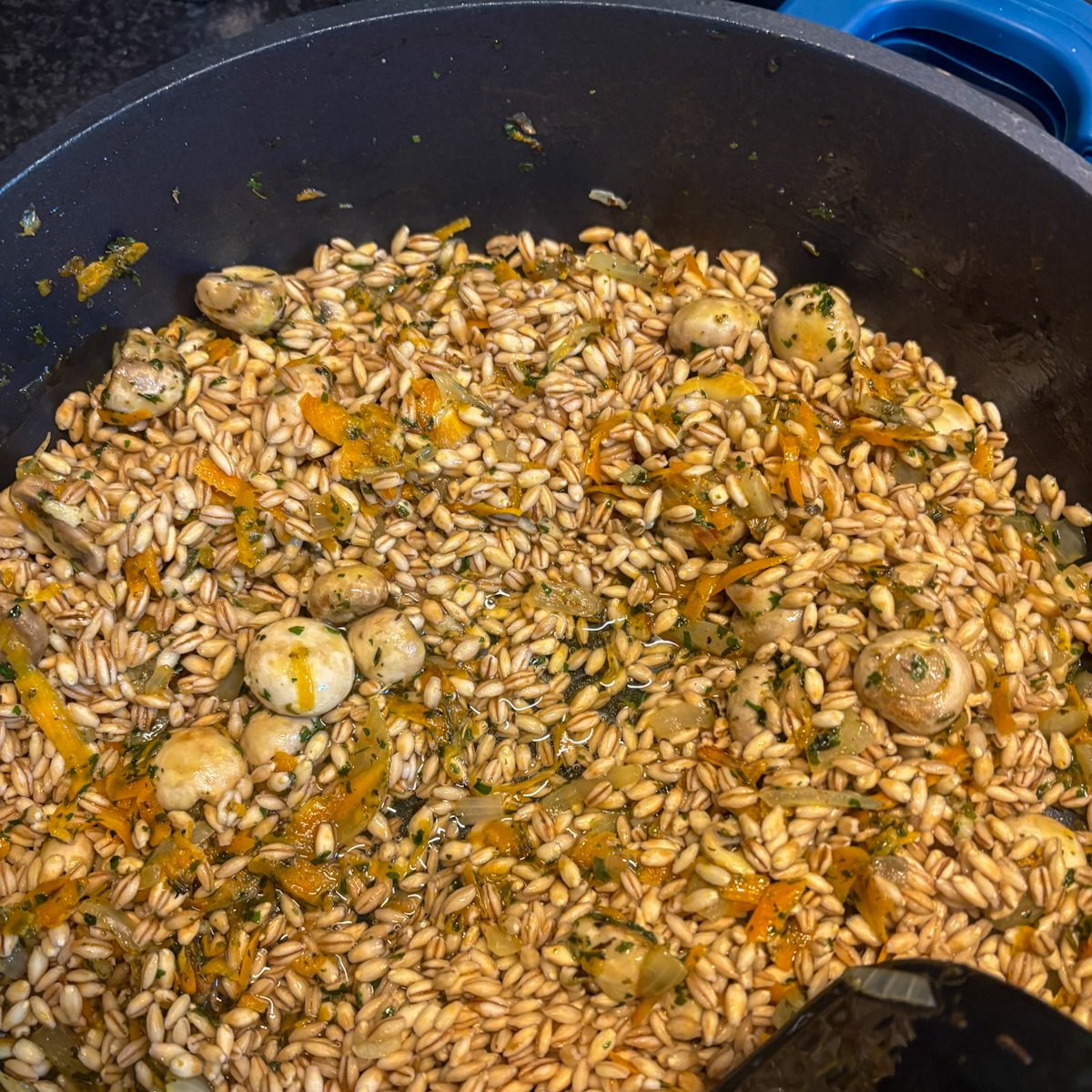 Pearl barley with mushrooms and carrots cooking in a pan before simmering