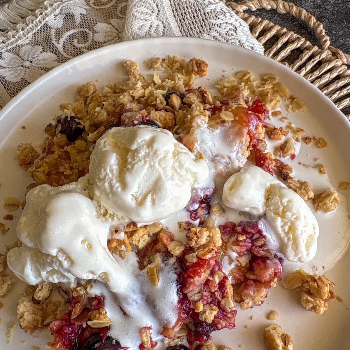 Plum and blueberry crumble with melting ice cream and syrupy plums on a plate