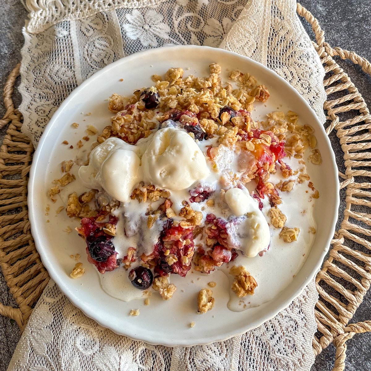 Plum and blueberry crumble with vanilla ice cream and juicy baked berries, overhead