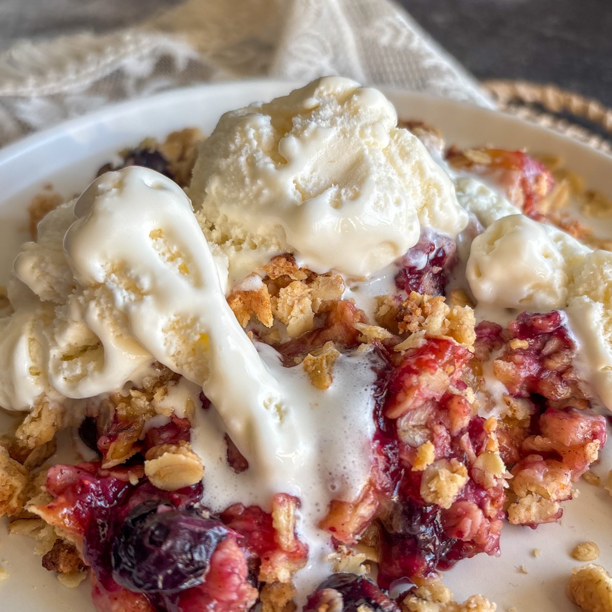 Close-up of plum and blueberry crumble with ice cream, oats and burst blueberries