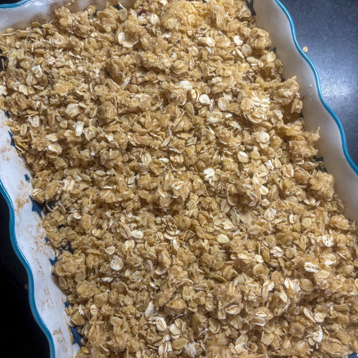 Unbaked plum and blueberry crumble with raw oat topping in a blue baking dish