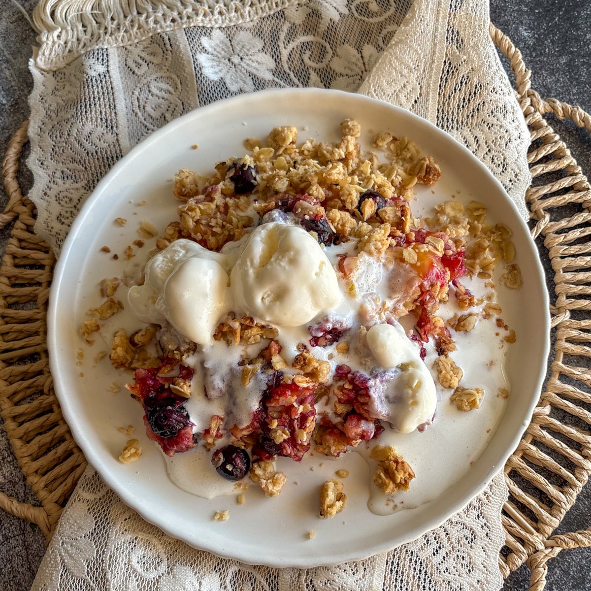 Plum and blueberry crumble with vanilla ice cream and golden oat topping, overhead