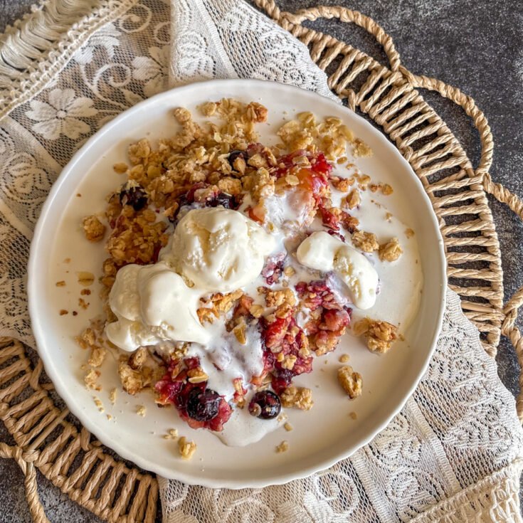 Plum and blueberry crumble with melting ice cream and golden oat topping on a white plate