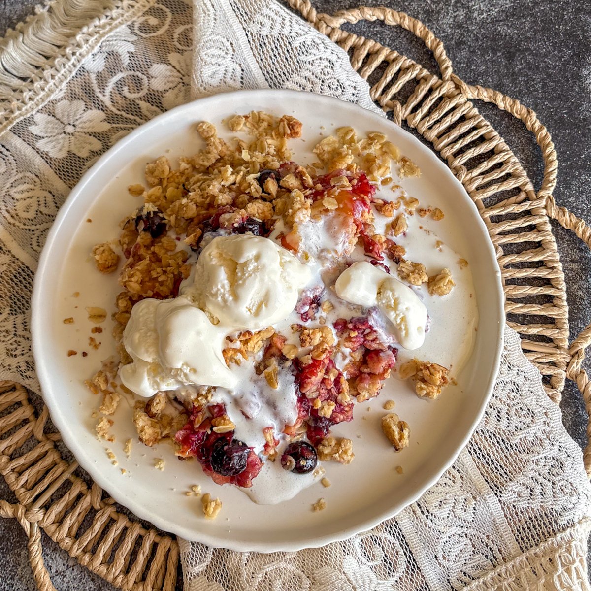 Plum and blueberry crumble with melting ice cream and golden oat topping on a white plate