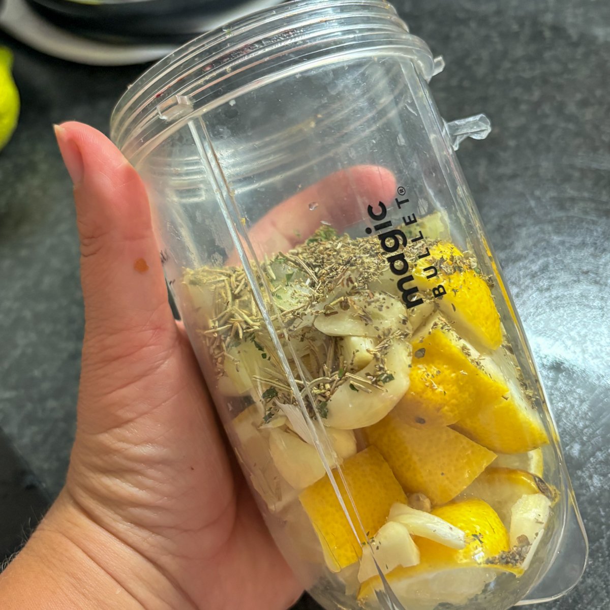 Whole lemon chunks, garlic cloves and dried herbs layered in a Magic Bullet blender cup, ready to blitz into the lemon garlic marinade for pork gigot chops.