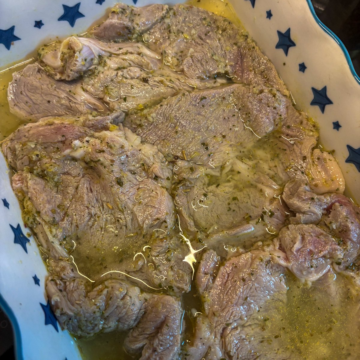 Marinated pork gigot chops resting in a star-patterned dish, glossy with lemon garlic marinade and olive oil, ready to braise in the oven.