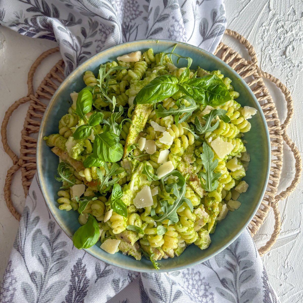 Rocket pesto pasta salad with chicken seen from above, spiral pasta tossed in creamy green pesto with rocket leaves and parmesan shavings scattered over the top