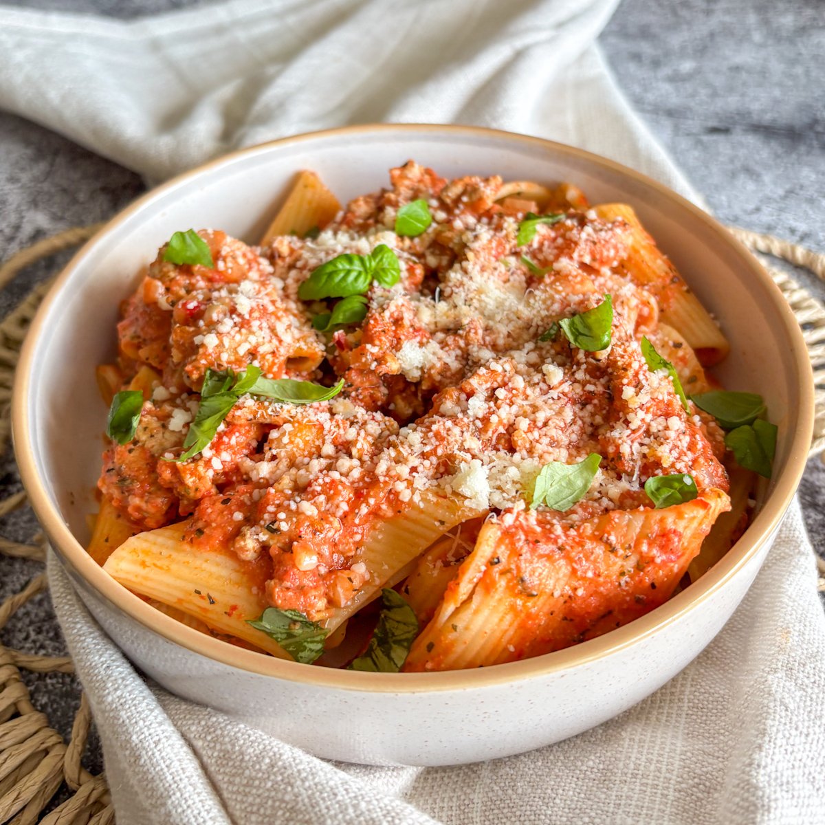 Side view of turkey and roasted pepper rigatoni topped with basil and a heavy dusting of parmesan