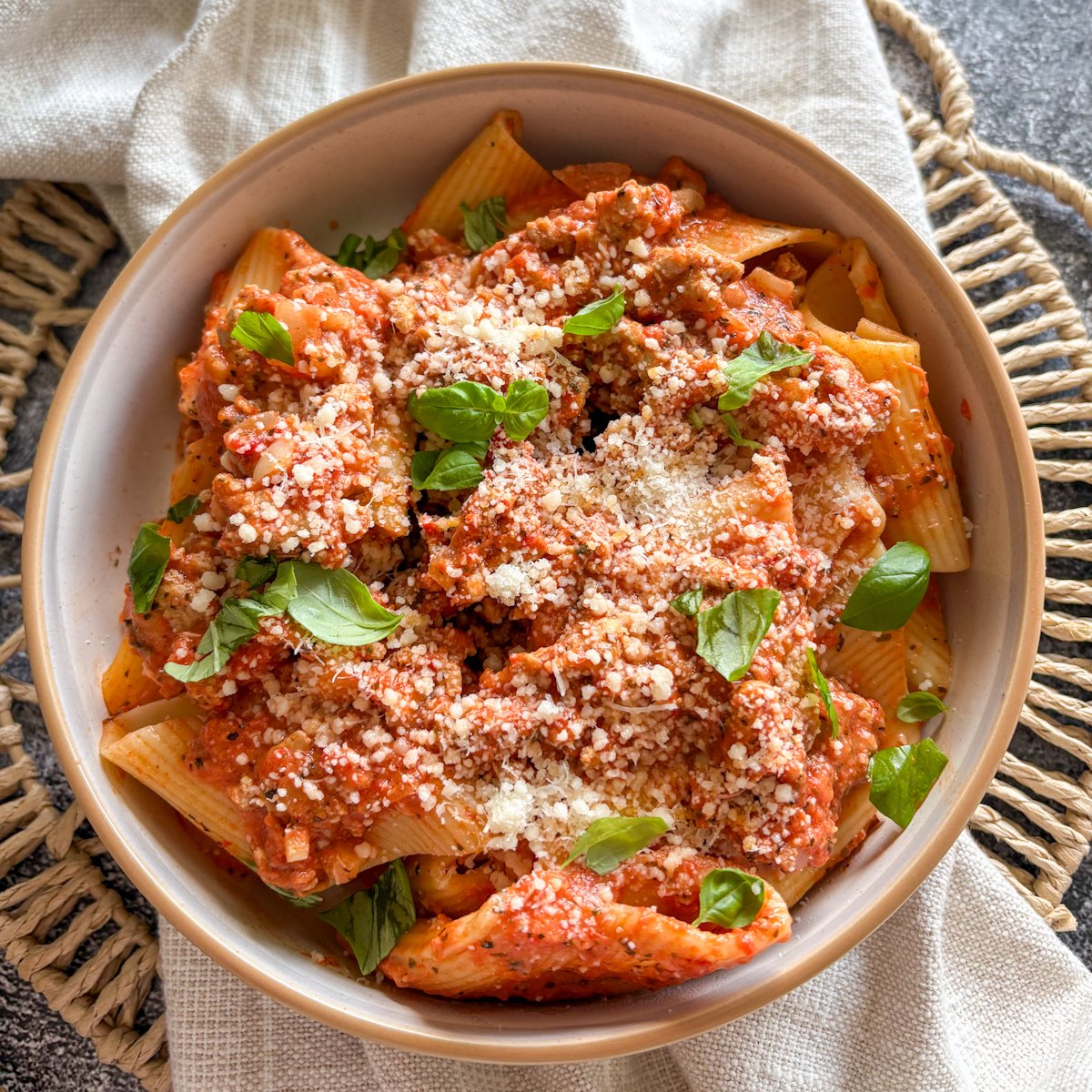 Overhead bowl of turkey and roasted pepper pasta with basil on a cream linen napkin