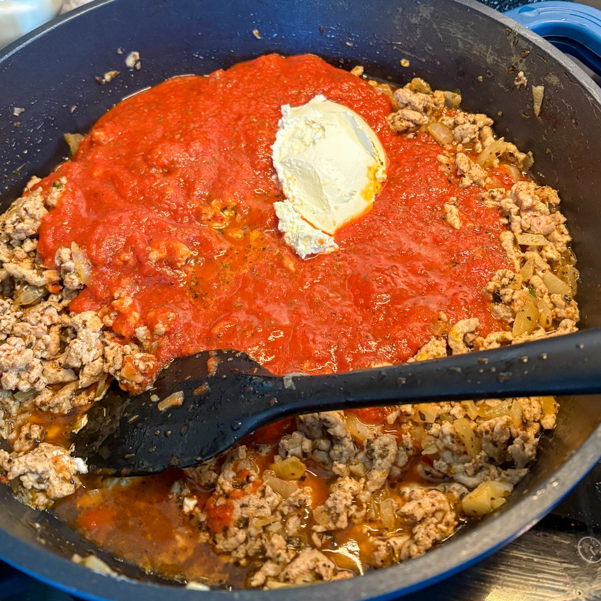Browned turkey mince with red tomato sauce and a spoon of cream cheese in a large pan