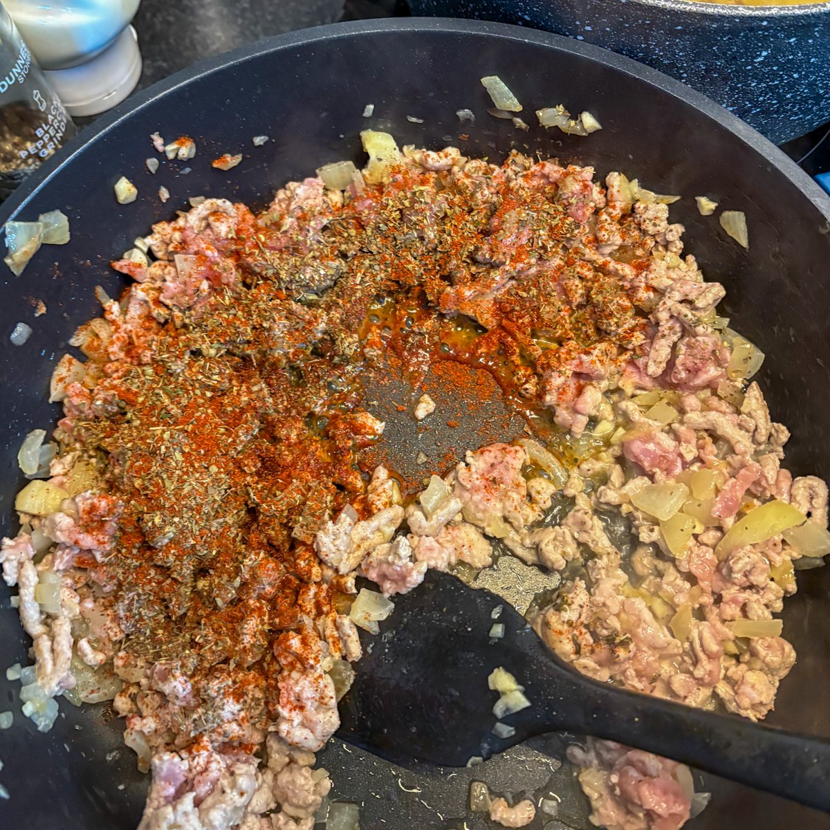 Turkey mince cooking with diced onion, paprika and herbs in a black skillet