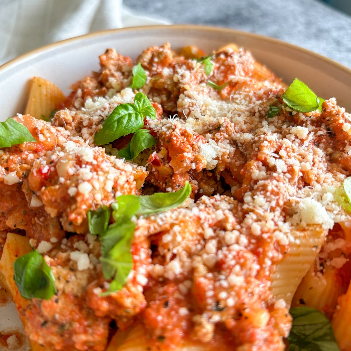 Close-up of creamy roasted pepper pasta with turkey mince, parmesan and fresh basil leaves
