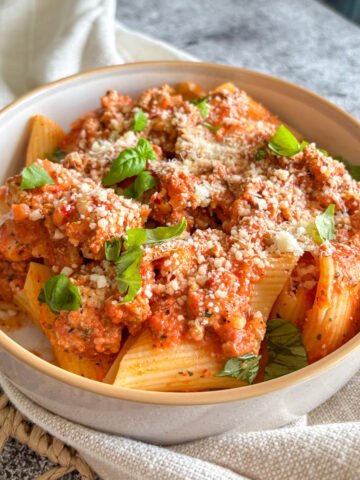 Close-up of creamy turkey rigatoni in roasted pepper sauce, topped with parmesan and a basil sprig