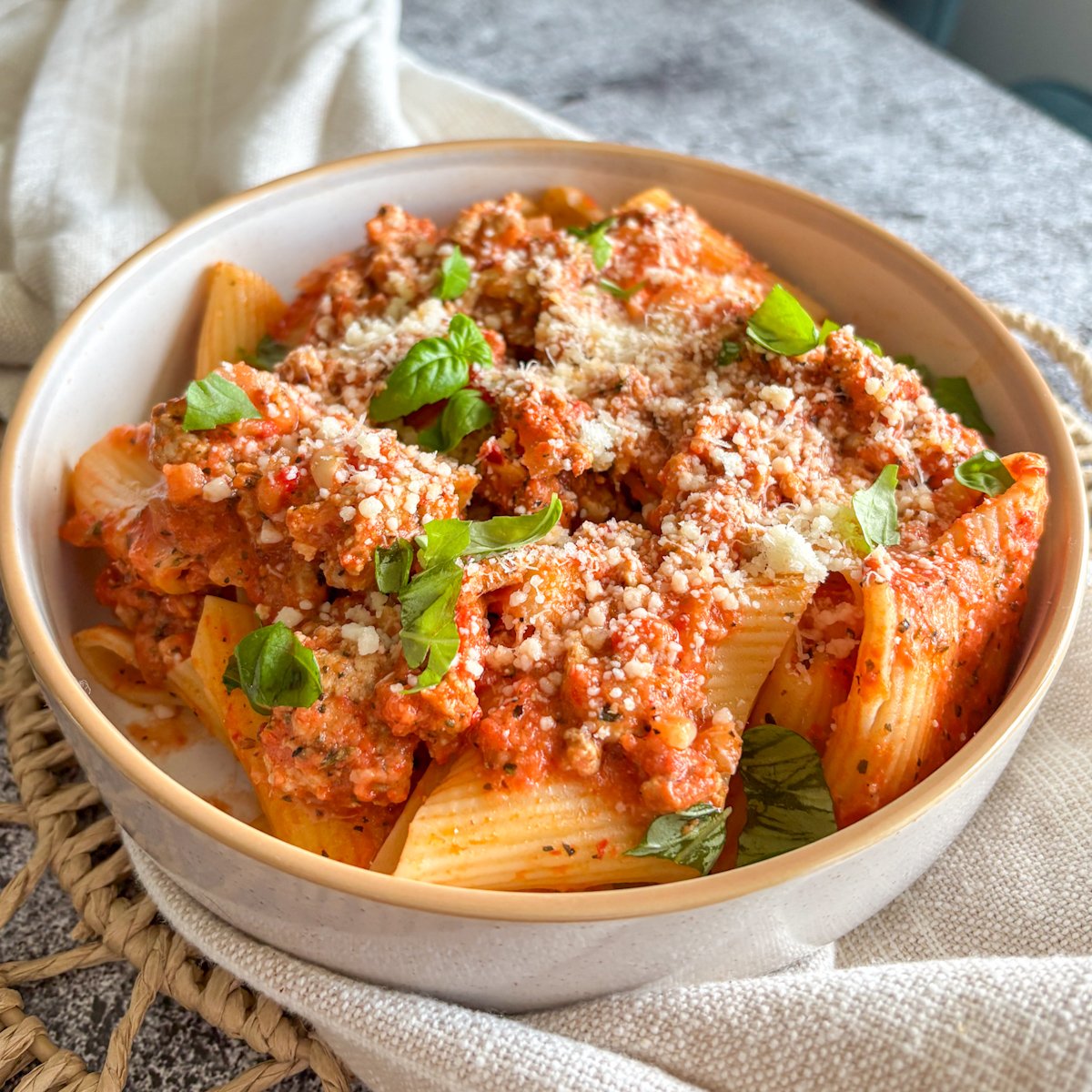 Close-up of creamy turkey rigatoni in roasted pepper sauce, topped with parmesan and a basil sprig