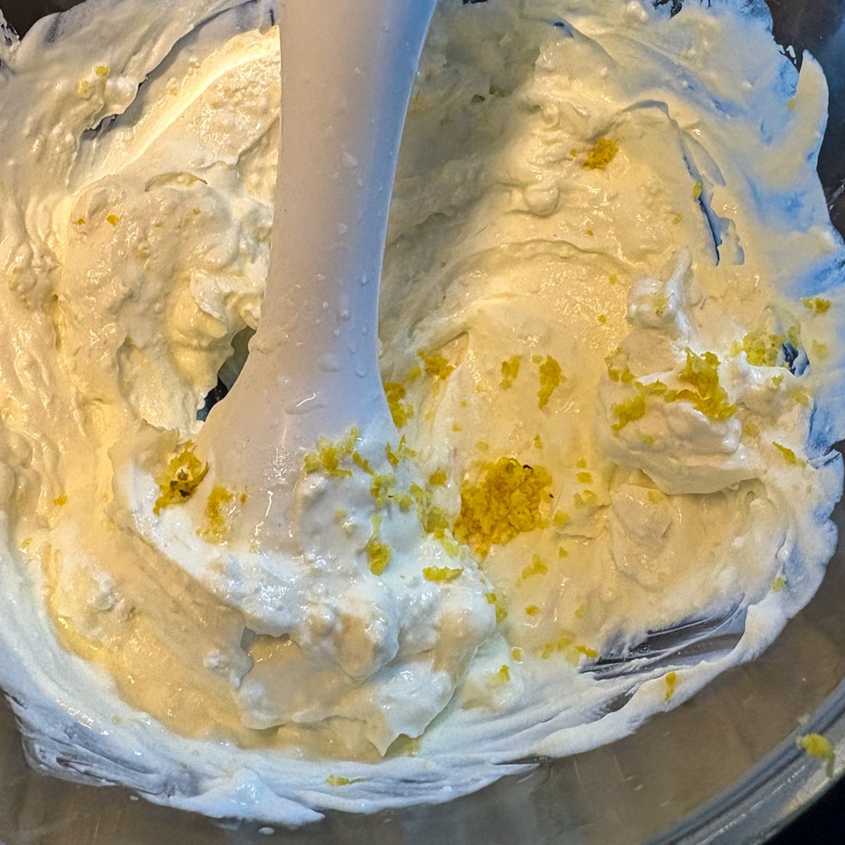 Whipped feta and Greek yoghurt blended smooth in a metal bowl with a hand blender, flecked with fresh lemon zest ready to be mixed through.