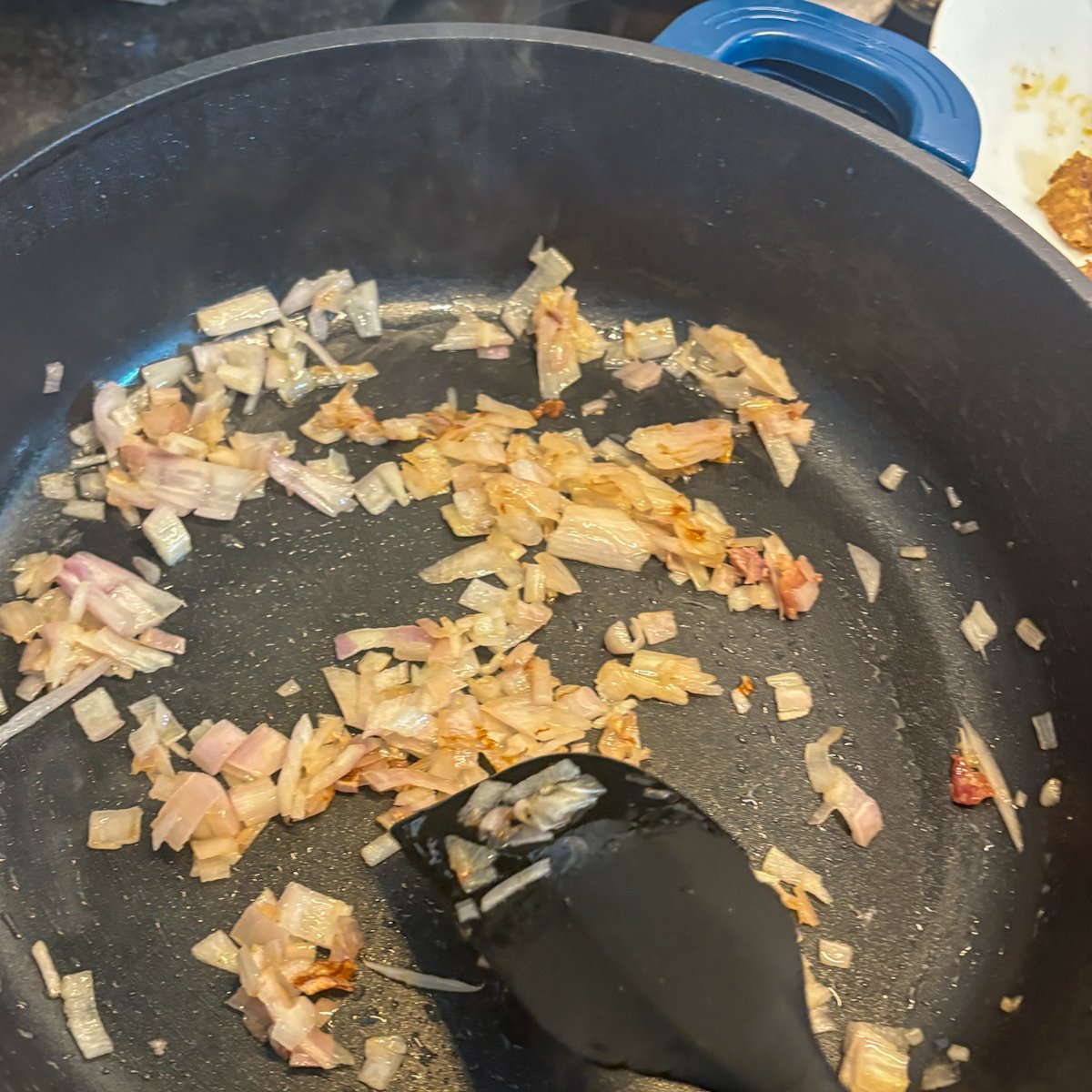 White beans and bacon prep – bacon offcuts frying crisp with onion in a black skillet