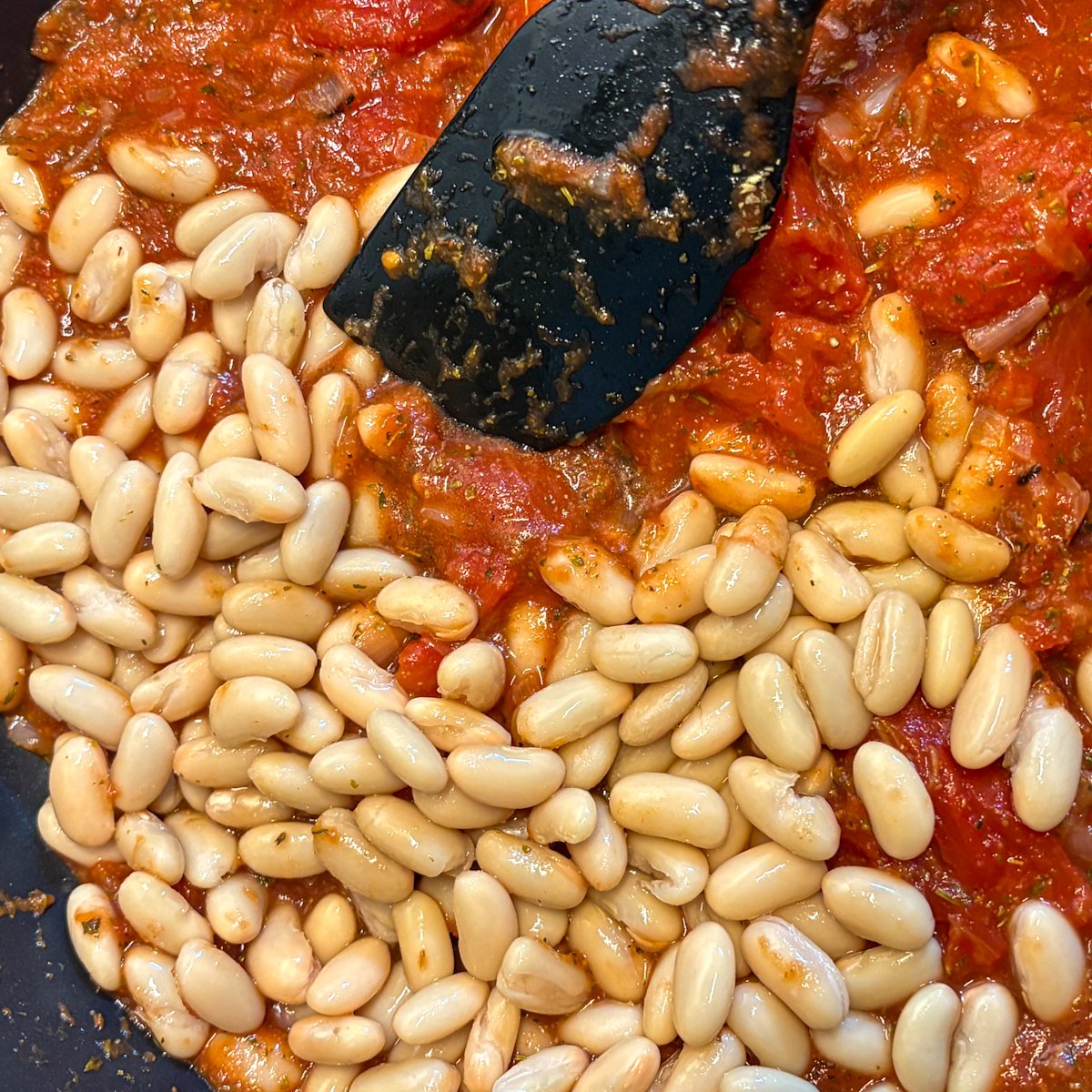  Cannellini beans added to tomato sauce in a skillet, ready to simmer with a spatula