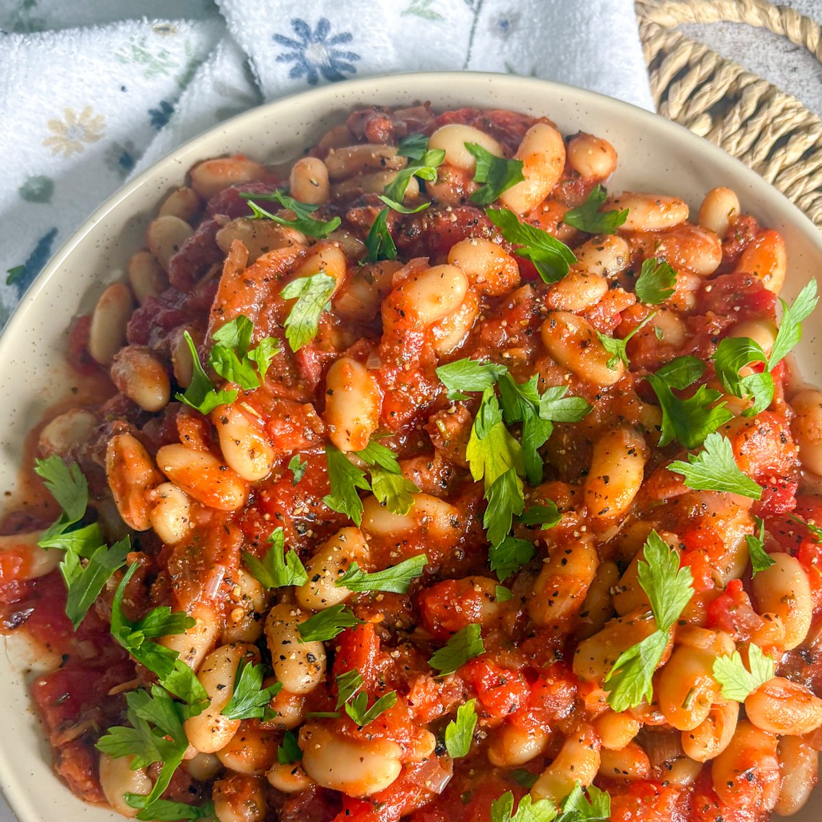 White beans and bacon in a creamy tomato sauce, close-up in a bowl with fresh parsley