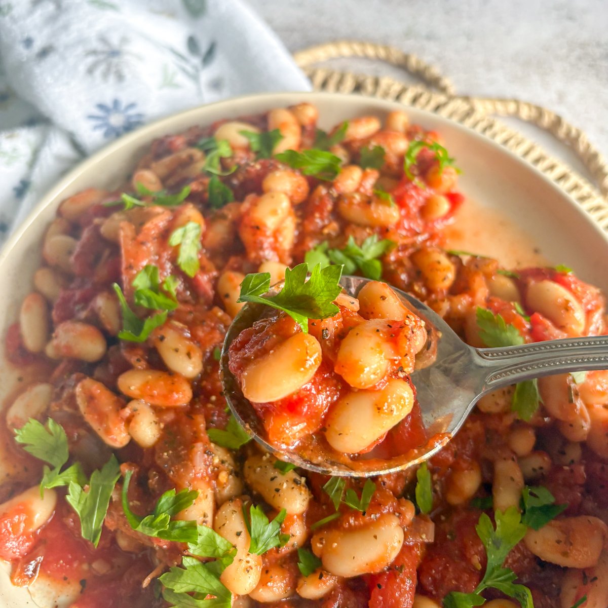 White beans and bacon in tomato sauce lifted on a spoon over a bowl, topped with parsley