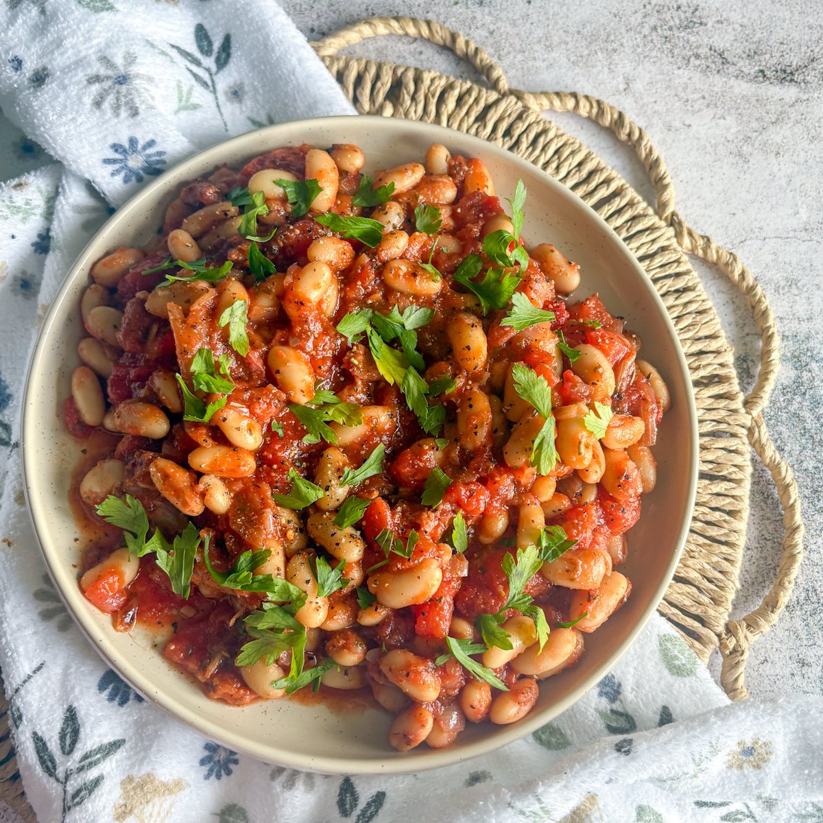  White beans and bacon in tomato sauce, overhead bowl with parsley on a woven mat